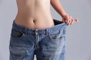 woman shows weight loss by wearing old jeans - (Weight Loss Surgery)